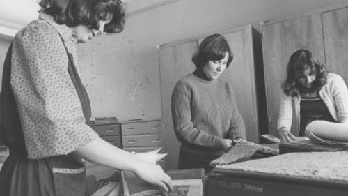 A black and white photo of three women in the Interior Design program looking through fabric samples