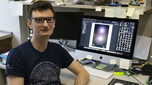 Photo of Astronomy professor, Dr. Michael Rutkowski in his office posing in front his computer with his NASA project viewable