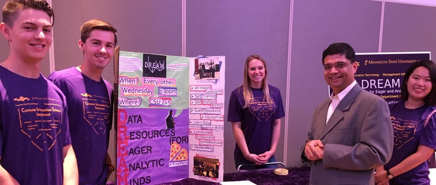the DREAM team, Data Resources for Eager and Analytical Minds, and professor posing at their table during the recognized student organization fair