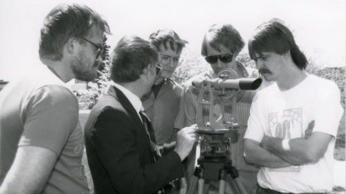 A black and white 1980s photo of a professor and students using survey equipment outside