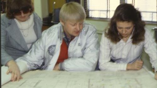 A Construction Management professor and two students looking at floor plans in the 1990s