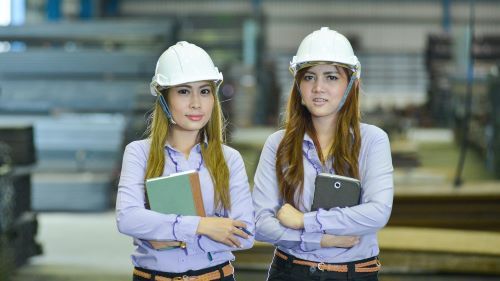 Two interns wearing safety helmets posing in the manufacturing warehouse
