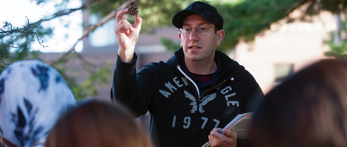 Biology instructor teaching outside holding a pinecone