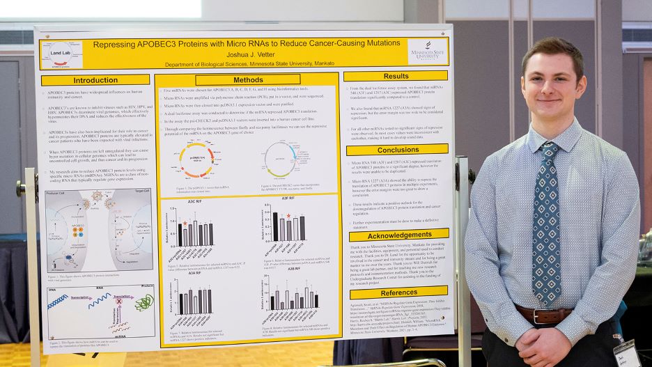 Josh posing next to his presentation board at the 2022 Undergraduate Research Symposium