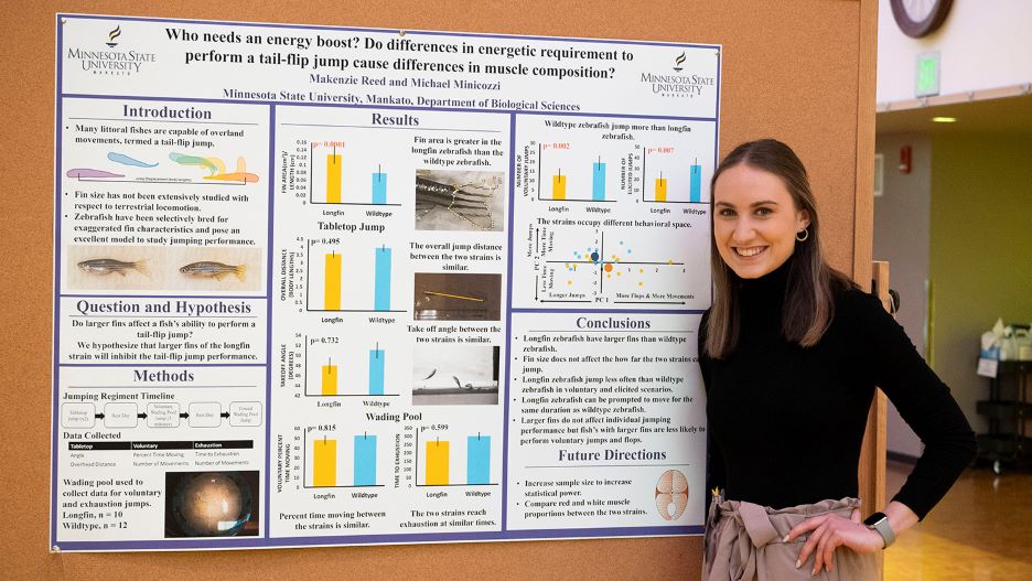 Kenzie posing next to her presentation board at the 2022 Undergraduate Research Symposium