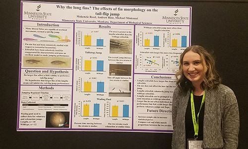 Makenzie Reed smiling while posing next to her zebrafish research poster
