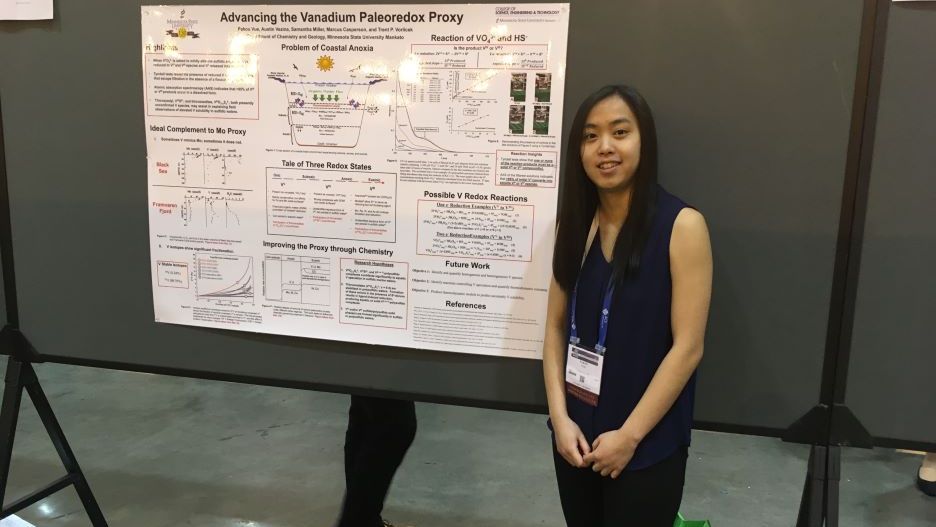 A student posing next to their research presentation board at the National Conference
