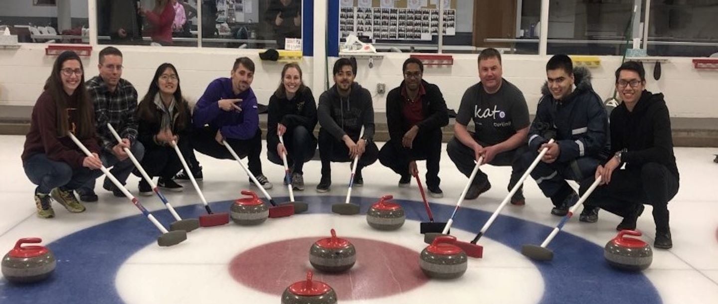 ACS club students sitting down with their curling broom and the stone posing inside on the ice