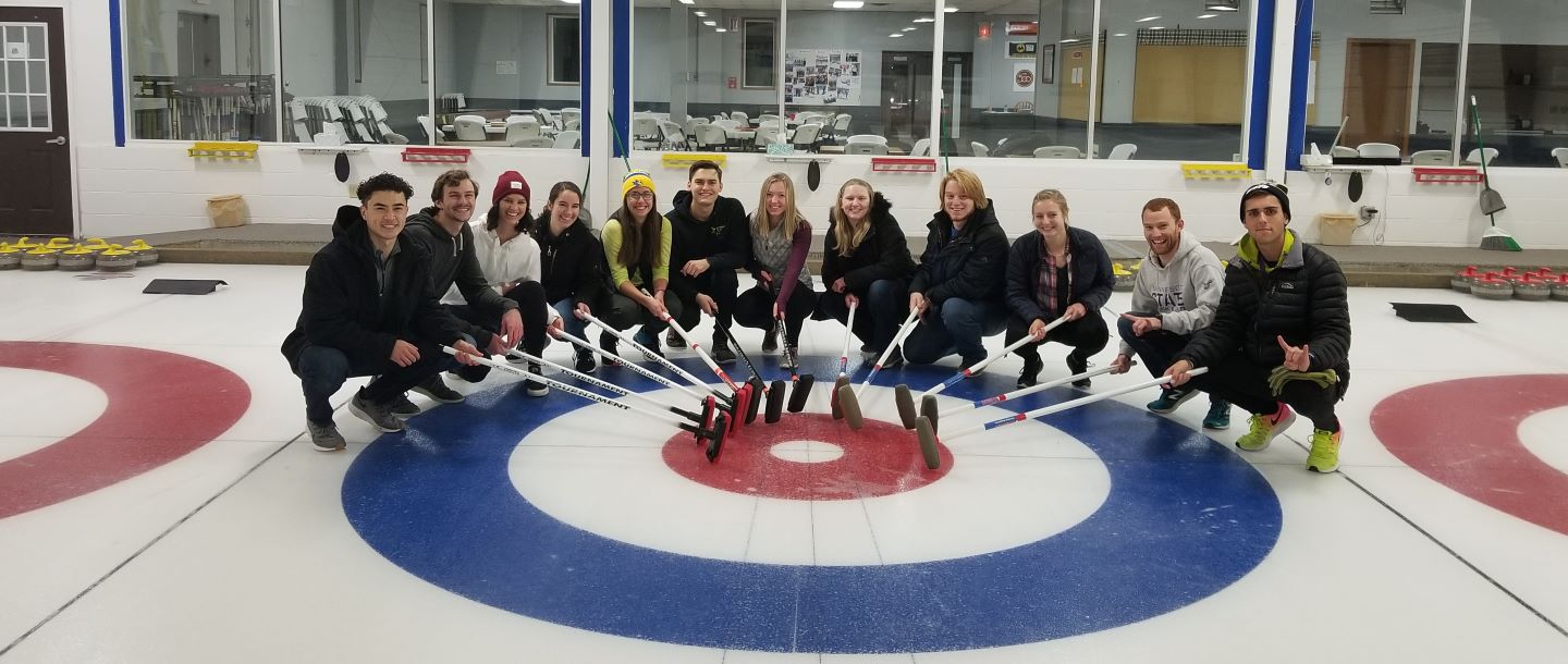 students with their curling brooms pointing at the targets posing inside on the ice