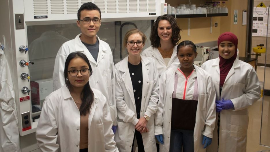 Students and instructor wearing white lab coats posing in the Katner lab