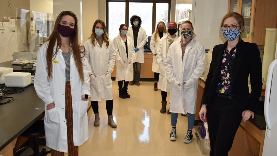 Students wearing white lab coats with the lab professor posing in the Katner laboratory