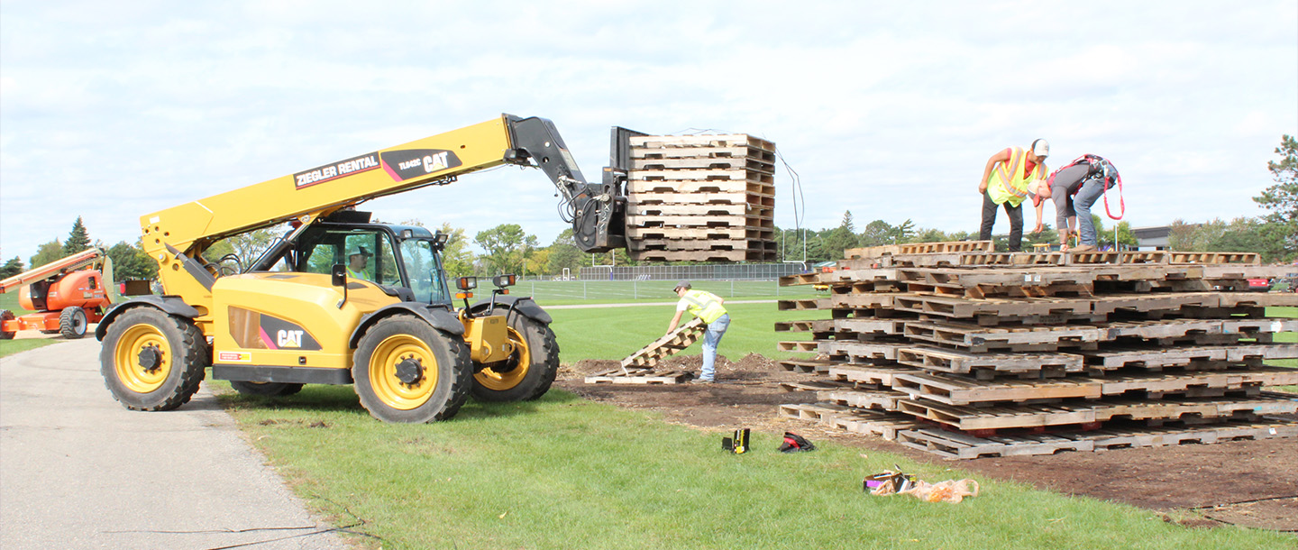 Construction Management students stacking wooden pallets on the field for the campus bonfire event
