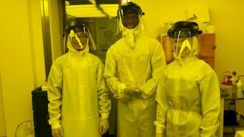 Students posing in the Microelectronics lab wearing protective lab suits