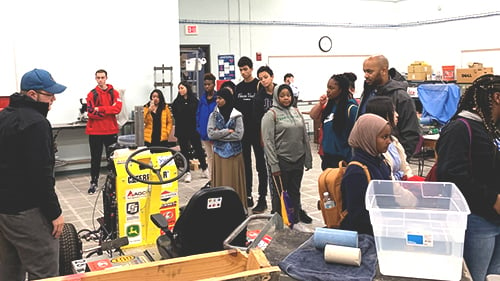 A group of students in the mechanical engineering lab viewing the designed competitive tractor during the African American Engineering Day