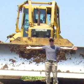 Aleigha Burg posing in front of a bulldozer with his arms spread out
