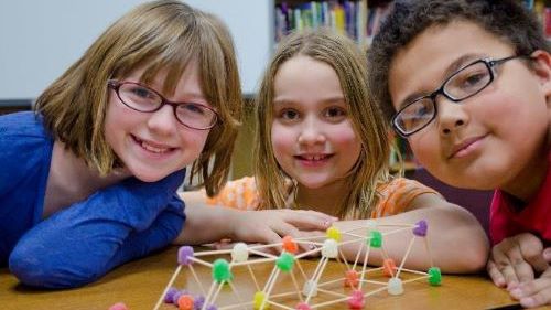 Three Elementary Engineering & LEAD students posing at a table with their bridge made from toothpicks and gumdrops