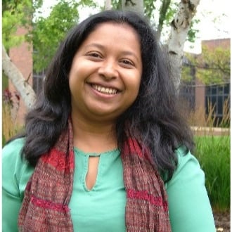 Maheshika Palihawadana posing with a smile outside on campus with trees and a building in the background